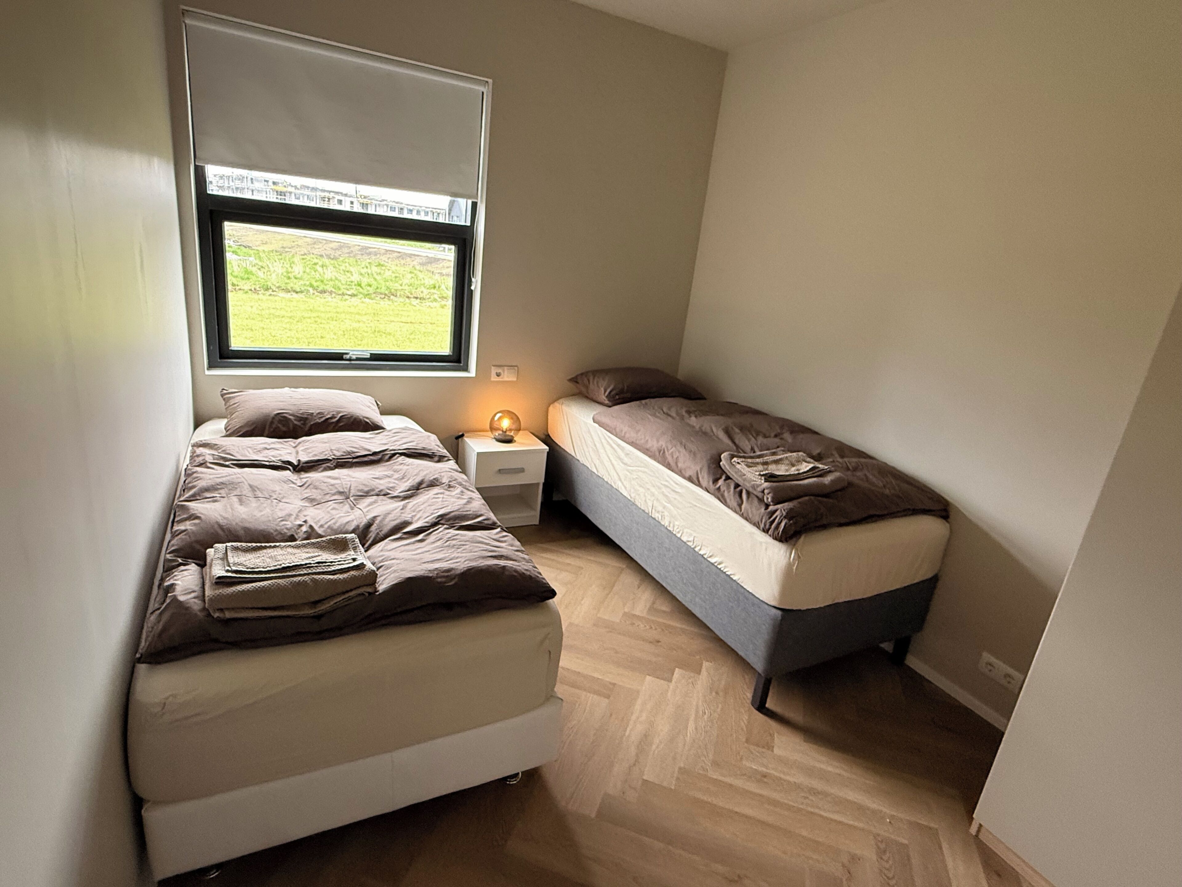 Ein kleines Zimmer mit zwei Betten, einem Fenster mit Blick auf eine Wiese und einem Nachttisch mit Lampe.