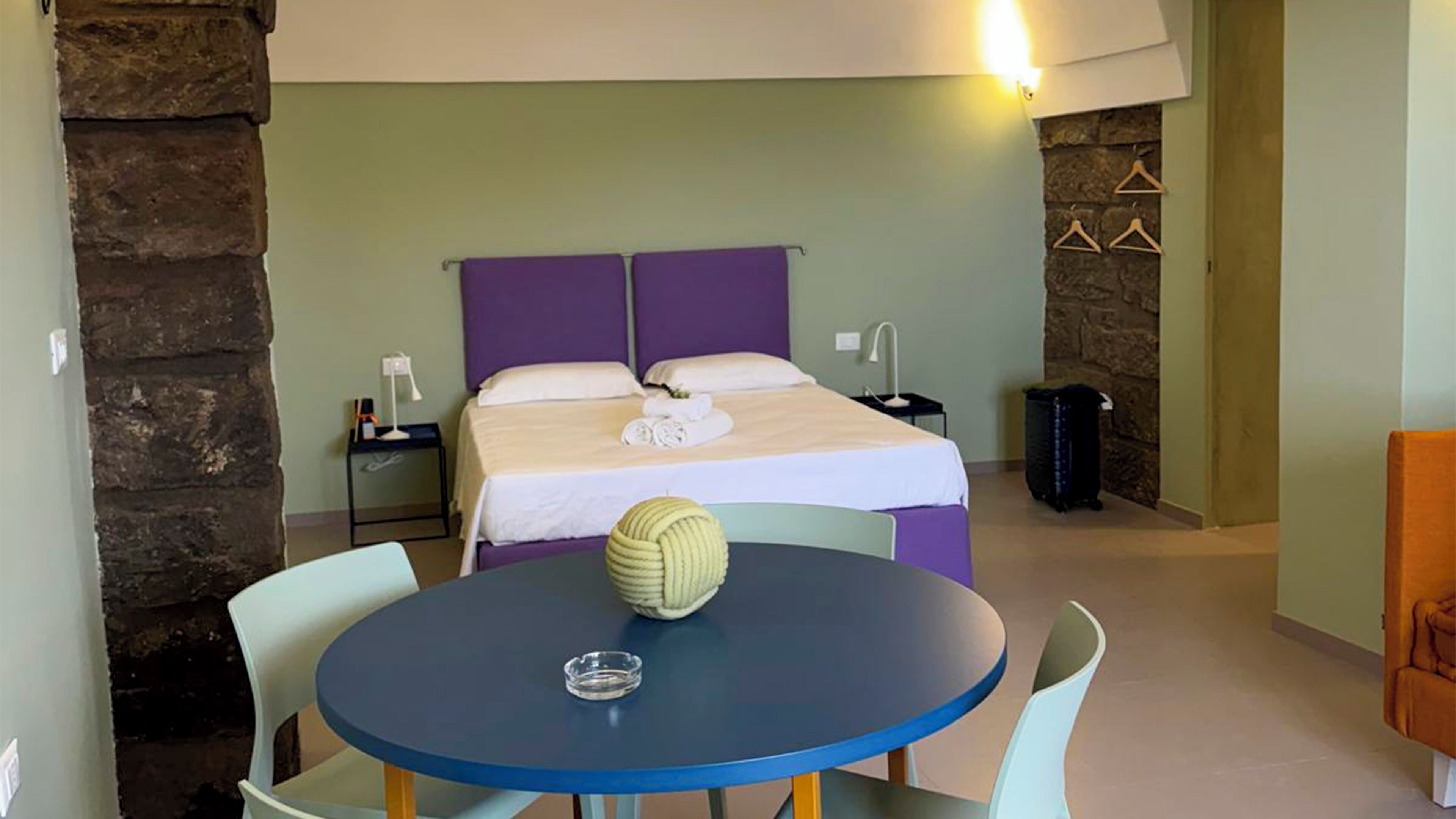 Ein Hotelzimmer mit Bett, Nachttischen, einem runden Tisch mit Stühlen und einer Steinwand.