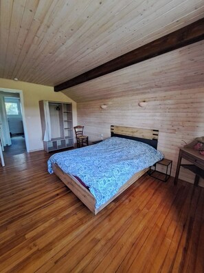Een slaapkamer met een houten plafond, een bed met een bedovertrek met dessin, een stoel en een kleine tafel.
