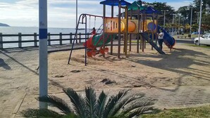 Ein Spielplatz mit Rutschen, Klettergerüsten, einem Sandbereich und einer Palme.