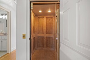 Ein schmaler Korridor mit einer Holztür am Ende, einem Lichtschalter an der Wand und einer weißen Tür auf der rechten Seite.