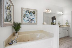 Ein Badezimmer mit einer großen Badewanne, einem Waschbecken mit Spiegel und zwei gerahmten Bildern an der Wand.