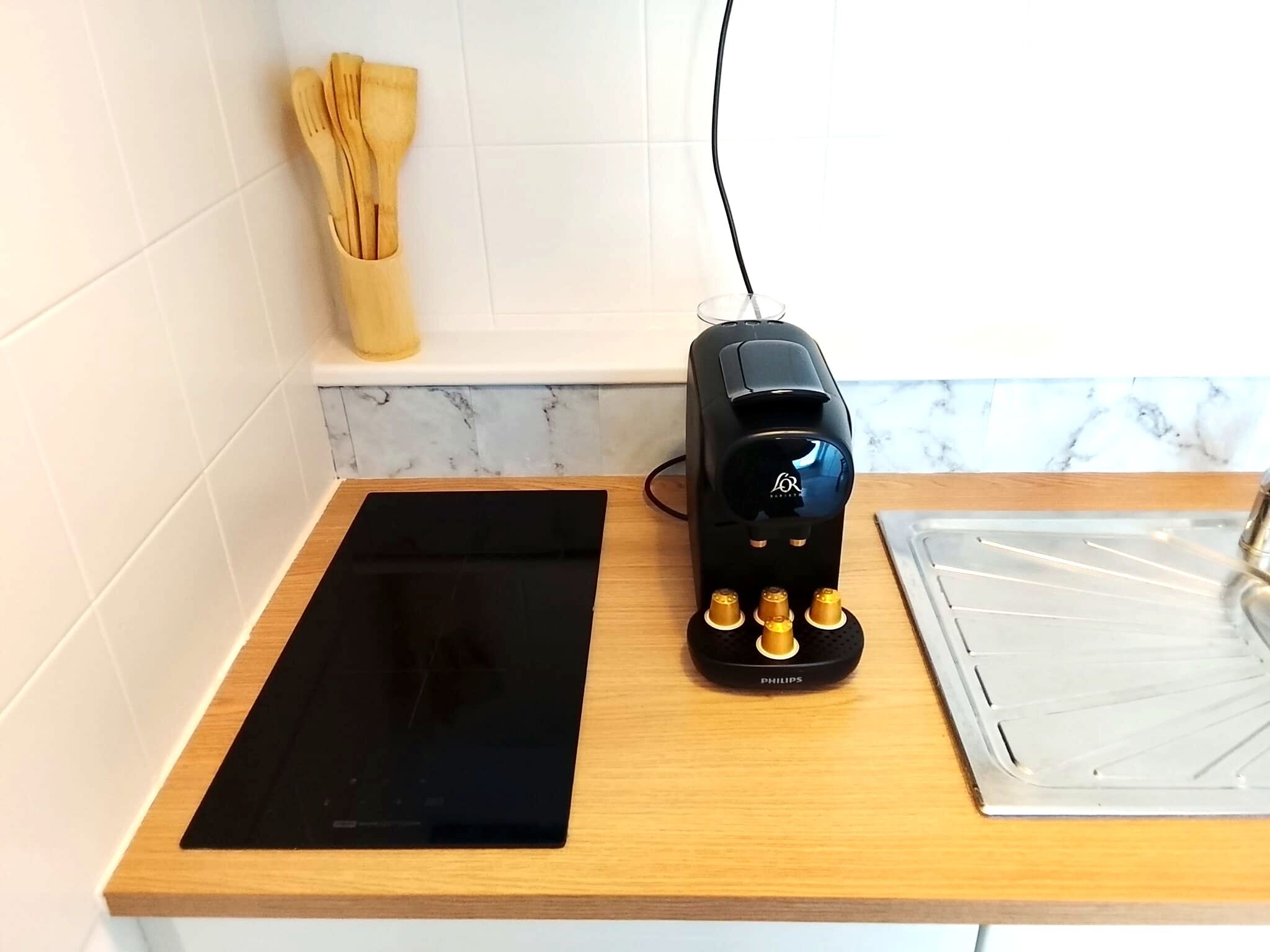 Eine Küche mit einer schwarzen Induktionskochplatte, einer schwarzen Kaffeemaschine und einer Marmor-Spritzschutzwand.