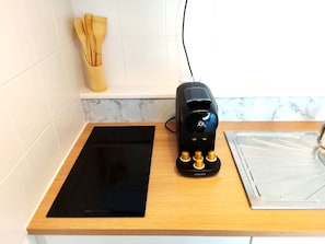 Ett kök med en svart induktionshäll, en svart kaffebryggare och en väggbeklädnad av marmor bakom arbetsbänken.