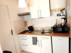 Ett kompakt kök med vita skåp, en diskho i rostfritt stål, en kaffebryggare, en mikrovågsugn och en vattenkokare.
