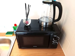 En svart mikrovågsugn med en genomskinlig glasbehållare ovanpå, en svamp och en flaska diskmedel på en bänkskiva i trä.