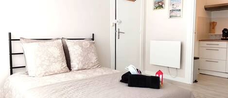 Un dormitorio con una cama, una mesita de noche con lámpara, una puerta y vistas a la cocina.
