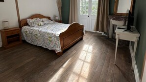 Une chambre à coucher avec un lit en bois, une table de chevet, un bureau avec une chaise, un miroir et une fenêtre avec des rideaux.