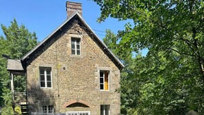 Un bâtiment en pierre avec un toit à pignon, une cour clôturée et une route dégagée devant.