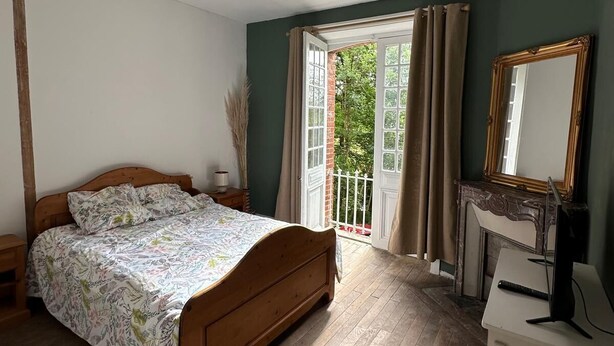 Une chambre avec un lit en bois, un bureau doté d’un miroir et une vue sur la verdure par la fenêtre.