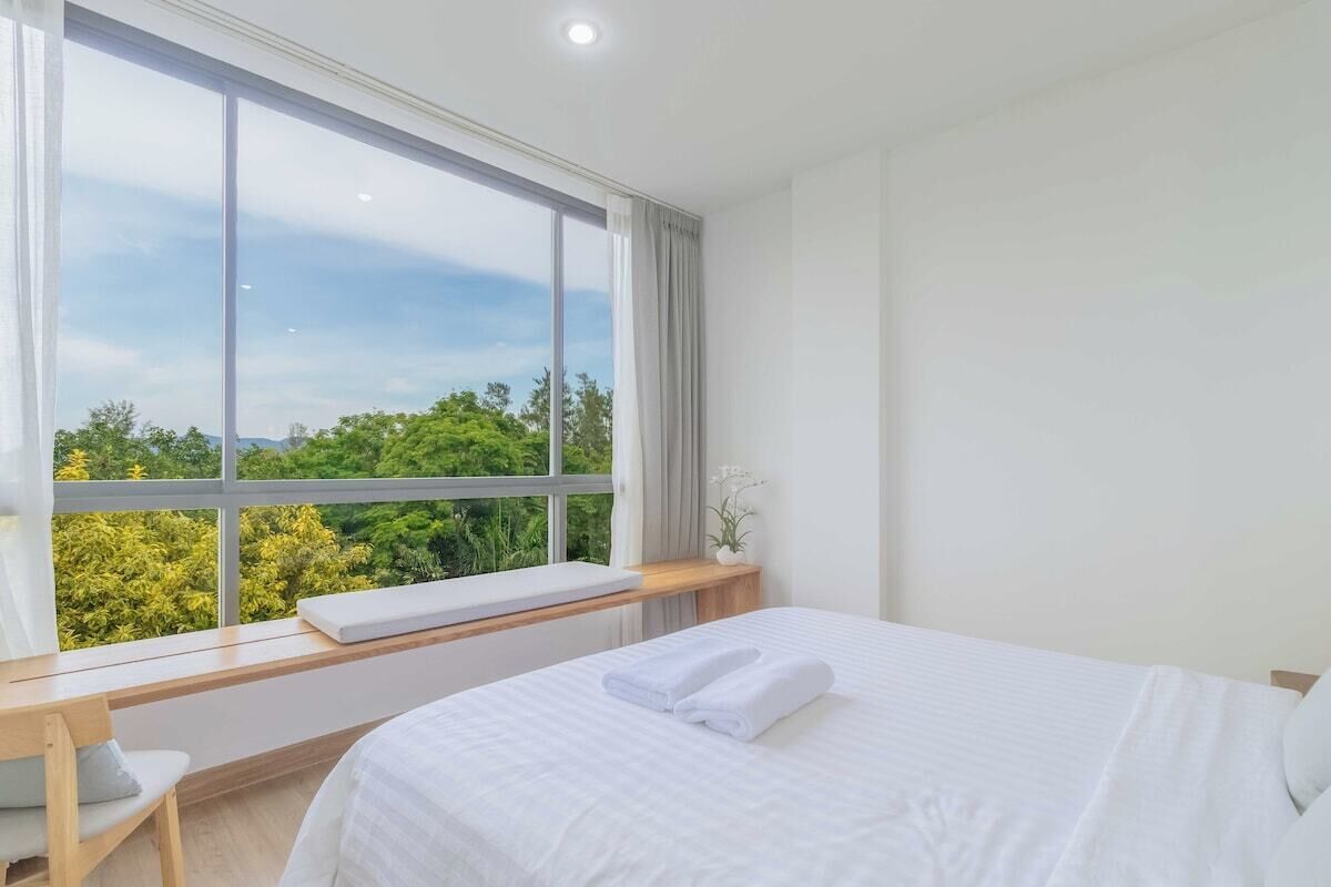 Ein Schlafzimmer mit großem Fenster, einem Bett, einem Nachttisch und einem Sessel.