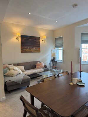 A living room with a sofa, a dining table, and a painting on the wall. - Spacious two bedroom, split level flat in the heart of Wandsworth. (London)
