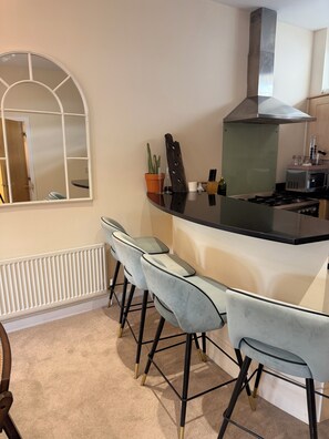 A modern kitchen with a central island, bar stools, a large window, and a built-in stove. - Spacious two bedroom, split level flat in the heart of Wandsworth. (London)