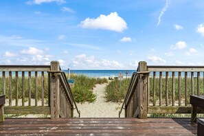Een houten terras dat naar een strand leidt, met een heldere lucht.