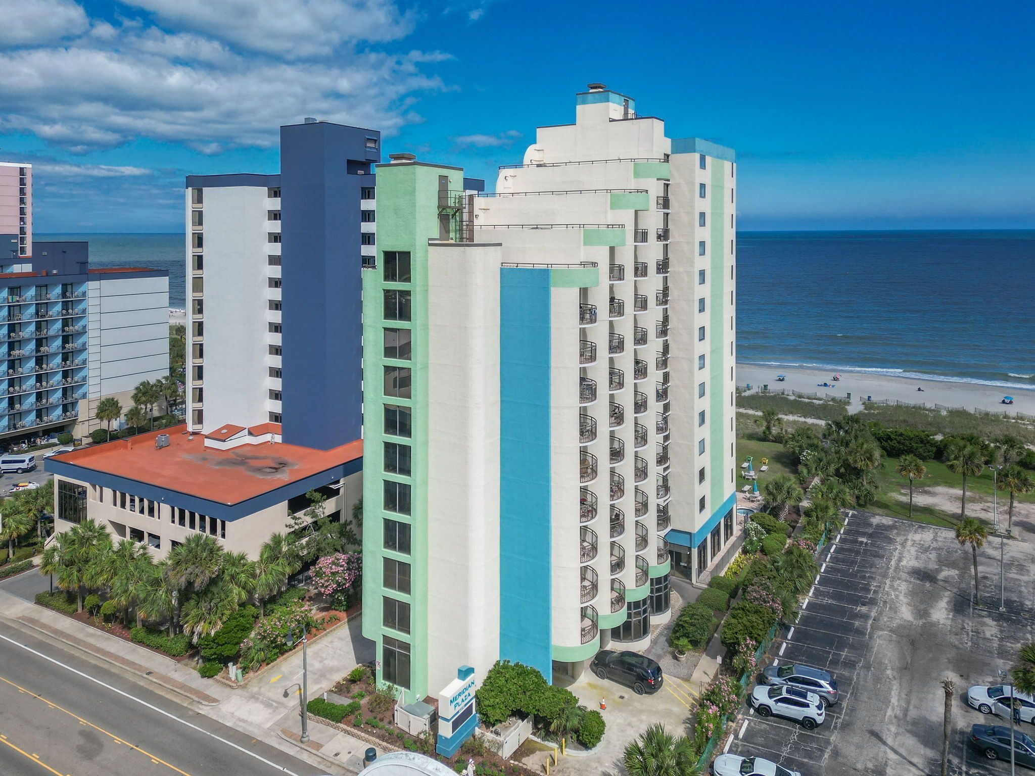 A multi-story hotel with a parking lot and a view of the beach.