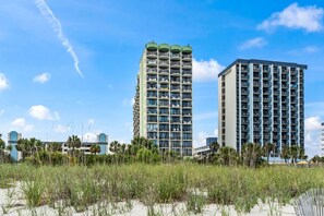 A high-rise hotel with multiple balconies, a beach in the foreground, and clear skies. - The Ocean Escape | Prime Myrtle Beach Getaway (Myrtle Beach)