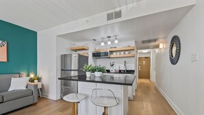 Een moderne keuken met een centraal eiland, barstoelen, een koelkast, een magnetron en een potplant.