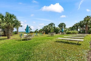 An outdoor seating area with tables and chairs, surrounded by palm trees and umbrellas. - The Ocean Escape | Prime Myrtle Beach Getaway (Myrtle Beach)