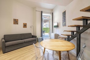 Ein modernes Wohnzimmer mit einem grauen Sofa, einem Holzespeisetisch, klaren Stühlen, einem Fernseher und einer Treppe.