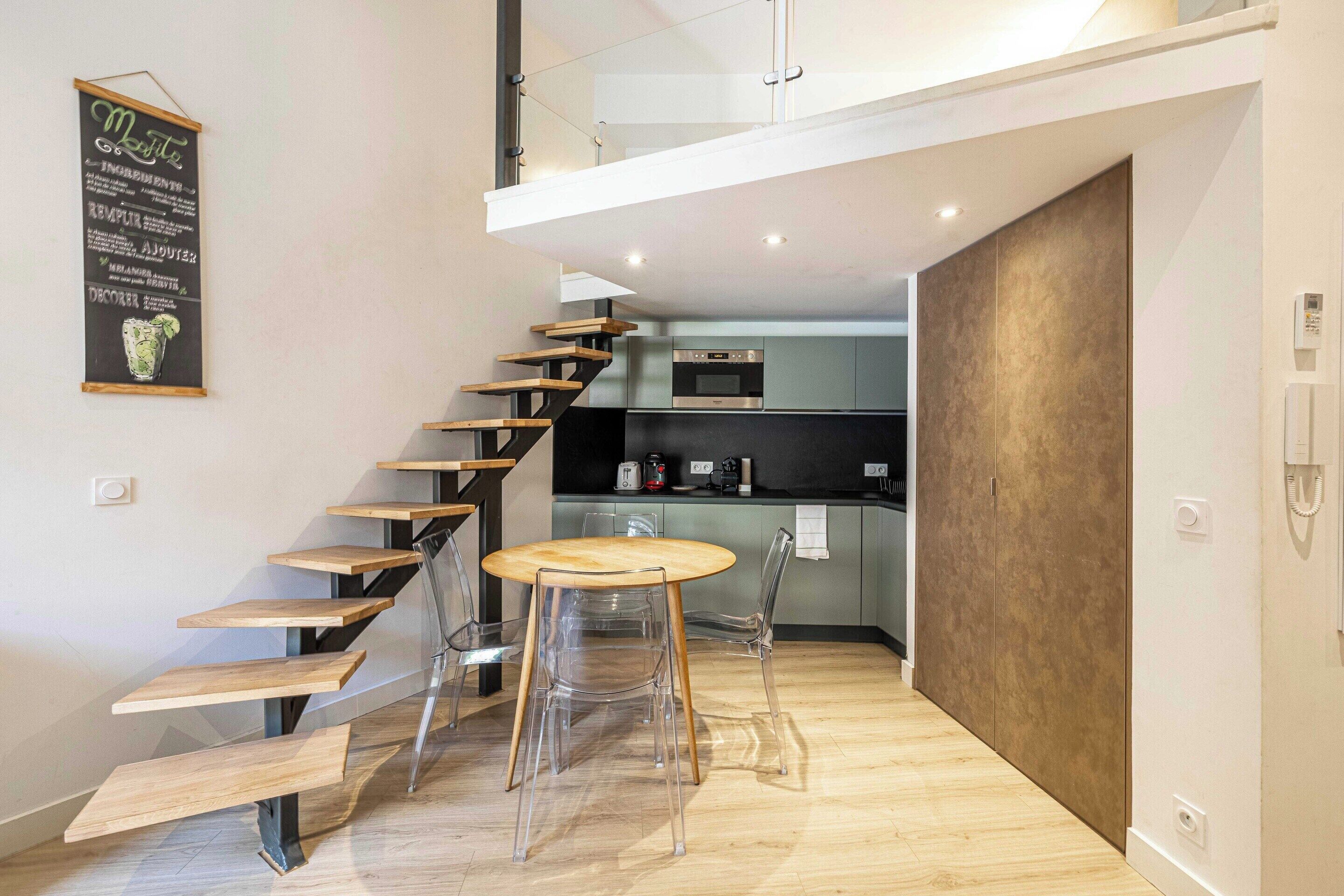 A modern kitchen with a wooden staircase leading to a loft.