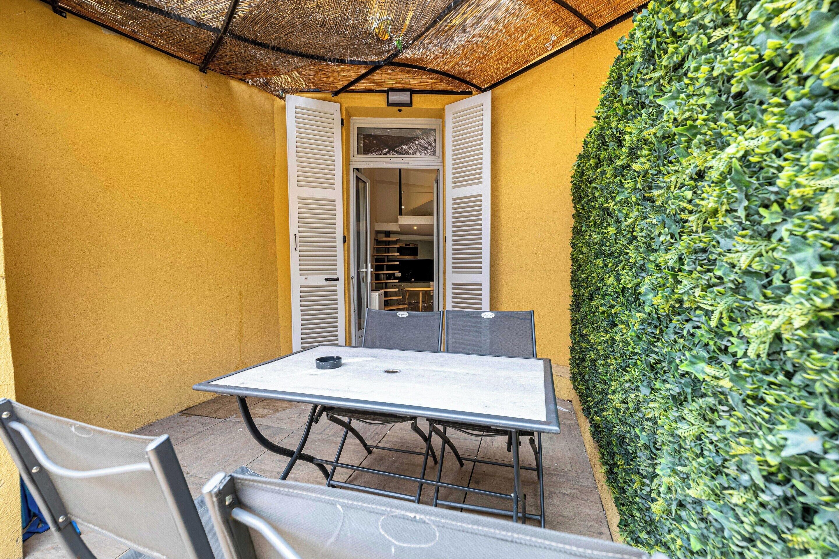 Une terrasse avec une table et des chaises, un toit de chaume et un mur végétal.