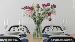 Uma mesa de jantar com um vaso transparente de flores, copos de vidro e pratos brancos.