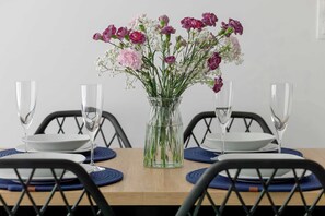 A dining table with a clear vase of flowers, clear glasses, and white plates. - Modern Studio with Air Conditioning | Close to the Beach (Mielno)
