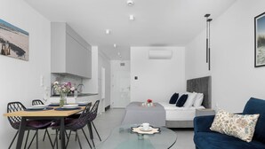 Uma sala de estar moderna com uma mesa de centro de vidro, um sofá azul e uma área de jantar com mesa e cadeiras de madeira.