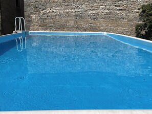 A clear blue swimming pool with a stone wall in the background.