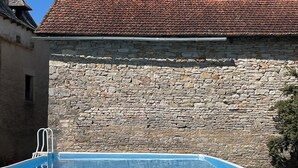 Une piscine avec un mur en pierre et un toit recouvert de tuiles, le tout sur fond de paysage.