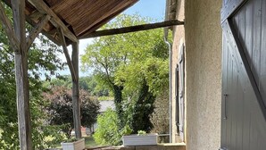 Une terrasse couverte avec une table, des murs en pierre et une vue sur la verdure.