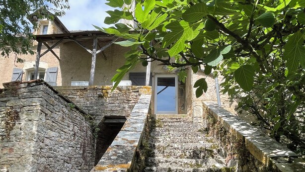 Un escalier en pierre menant à l’entrée d’un bâtiment, entouré de verdure et de murs en pierre.