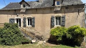 Un bâtiment en pierre avec un escalier menant à une porte, le tout entouré de verdure.