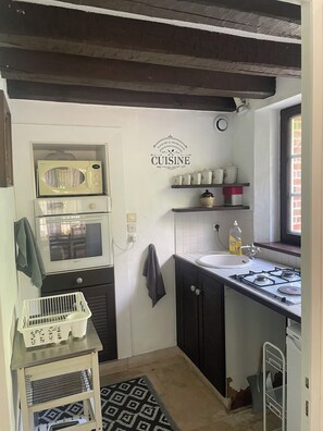A kitchen with a microwave, stove, sink, and a wall-mounted shelf with kitchenware. - A charming old barn (Coullons)