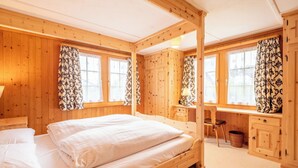 A wooden cabin bedroom with a bed, desk, chair, and windows.
