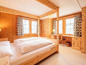 A wooden cabin bedroom with a bed, desk, chair, and windows.