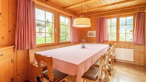 A wooden room with a long table, chairs, and large windows with curtains.