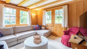 A cozy room with a sectional sofa, a round ottoman, and a red plaid chair.