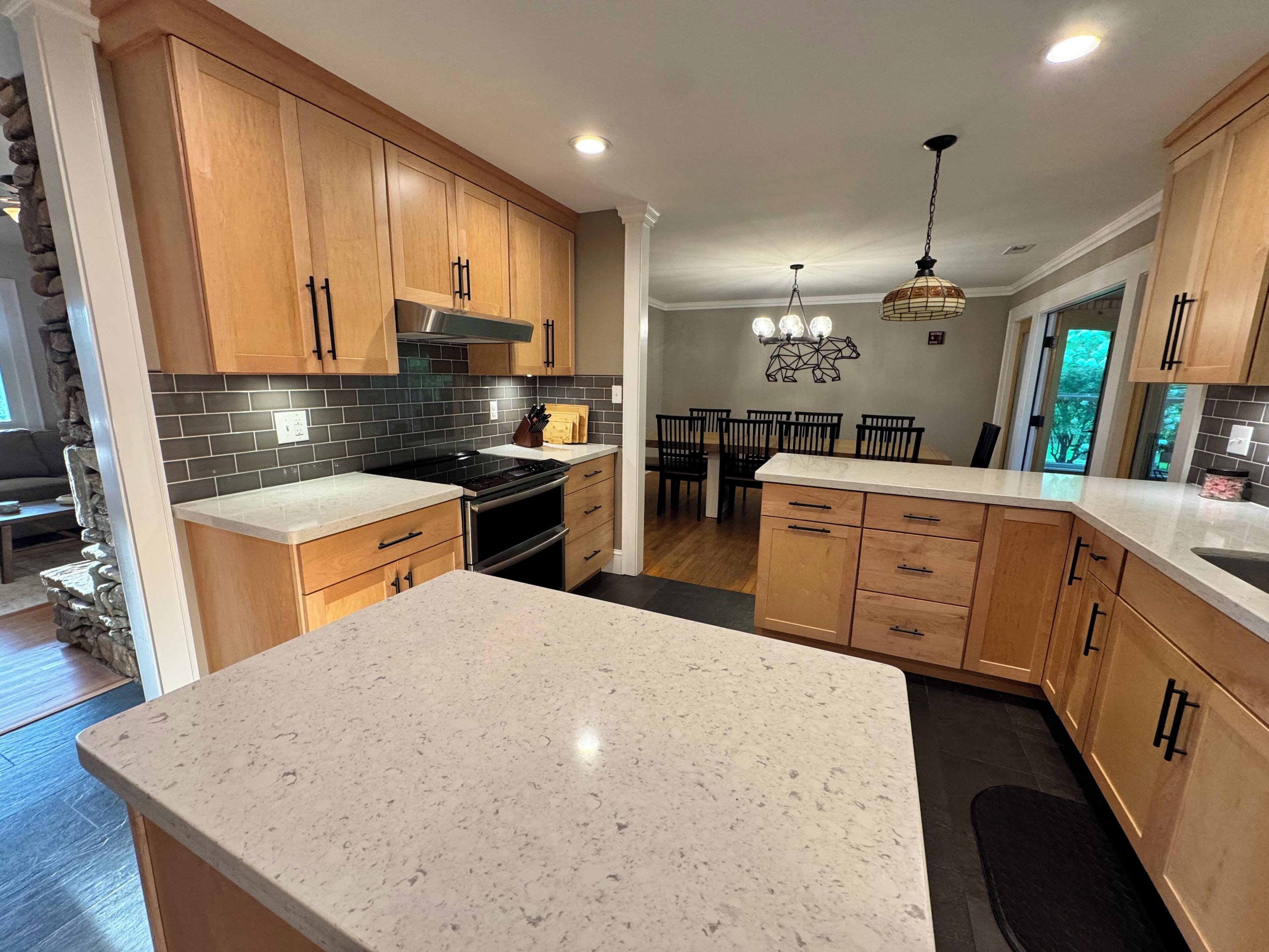 A modern kitchen with wooden cabinets, a granite countertop, and a dining area with a chandelier.