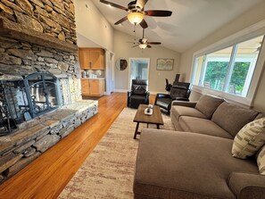 A living room with a stone fireplace, leather chairs, a sofa, and a large window.