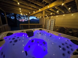 A hot tub with multiple jets, surrounded by a wooden deck and string lights.