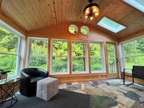 A room with wooden walls, large windows, a black leather chair, a cushioned ottoman, and a stone-patterned floor.