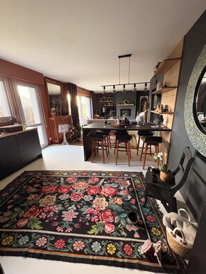A modern kitchen with a central island, wooden chairs, and a large floral rug. - A beautiful, spacious house near the ocean (Ploemeur)