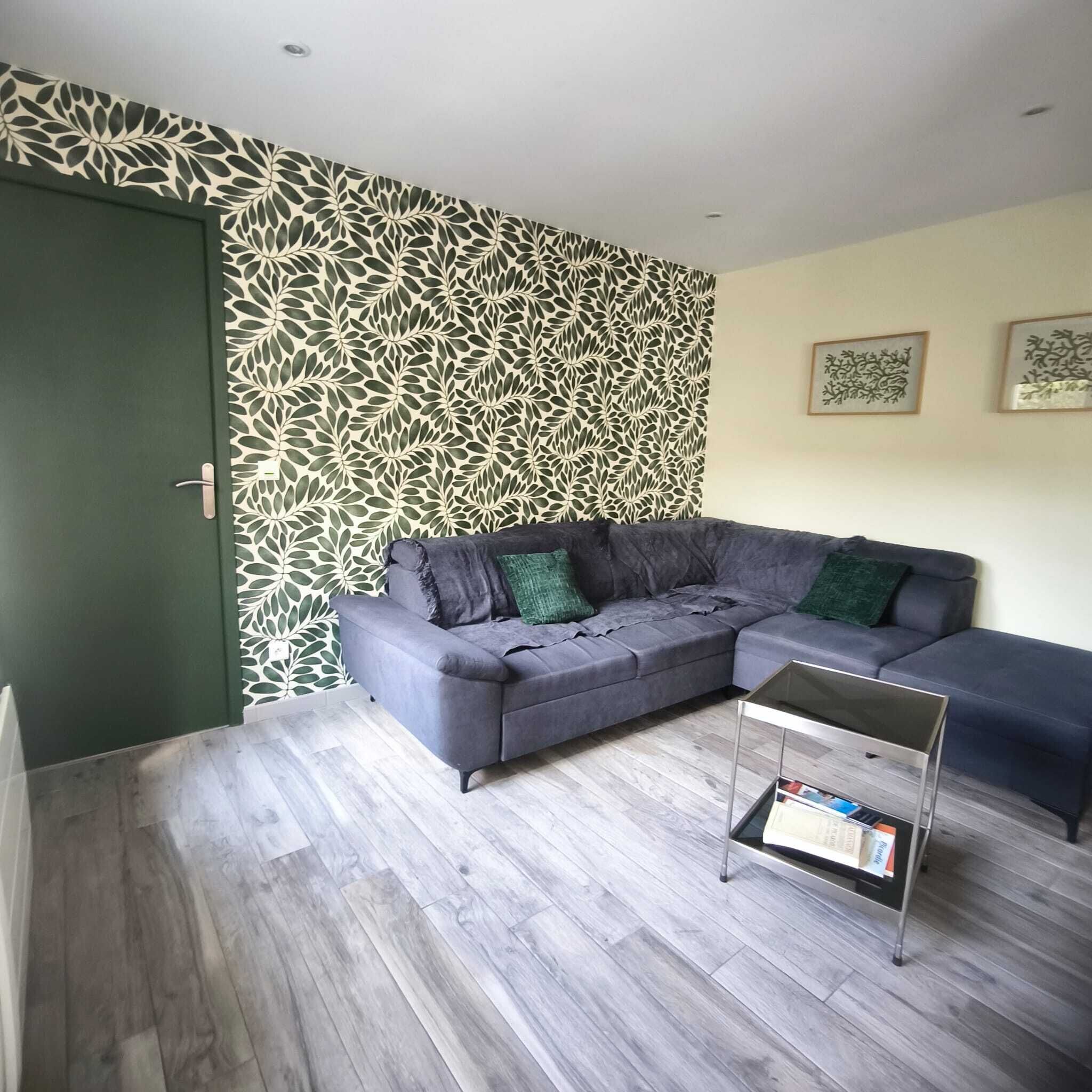 Un salon moderne avec un canapé d’angle gris, une petite table d  ’appoint et un papier peint à motifs.