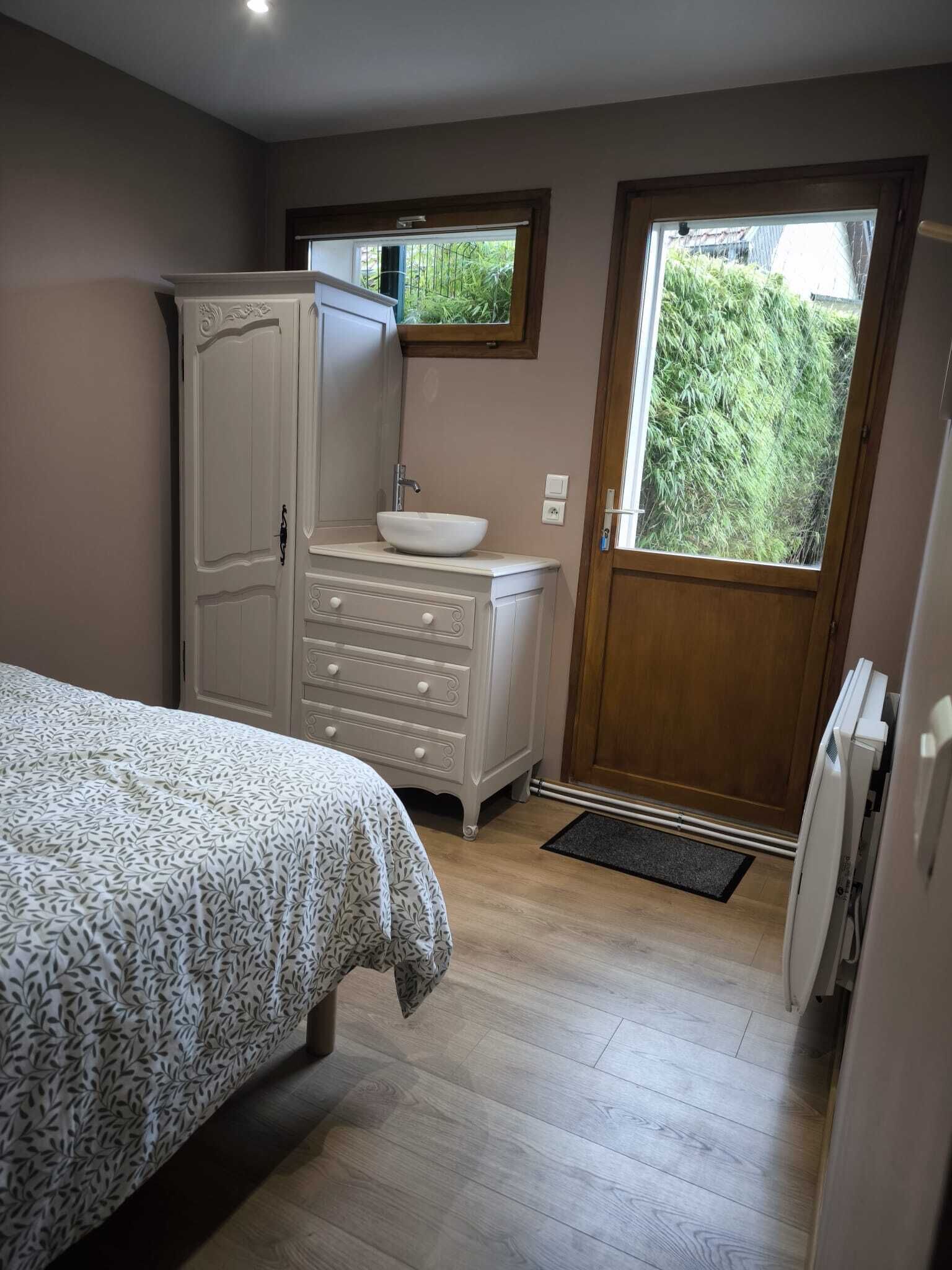 A bedroom with a bed, a dresser, a sink, and a window with a view of greenery.