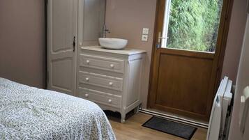 A bedroom with a bed, a dresser, a sink, and a window with a view of greenery.