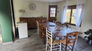 Een eetgedeelte met een houten tafel en stoelen, een klok aan de muur en een raam met gordijnen.