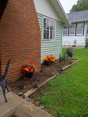 A house with a brick exterior, a green door, and a flower bed with autumn flowers.