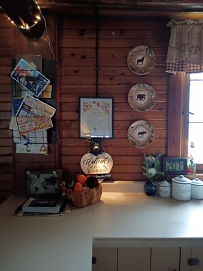 A cabin interior with a welcome sign, a framed menu, a world map, a fruit bowl, and a digital clock.