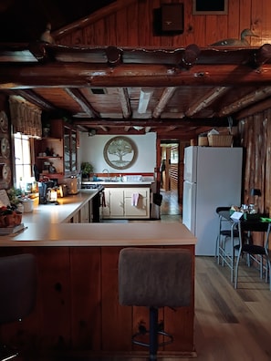 Une cuisine rustique avec des poutres en bois, un îlot central doté de tabourets de bar, un réfrigérateur et un évier fixé au mur.